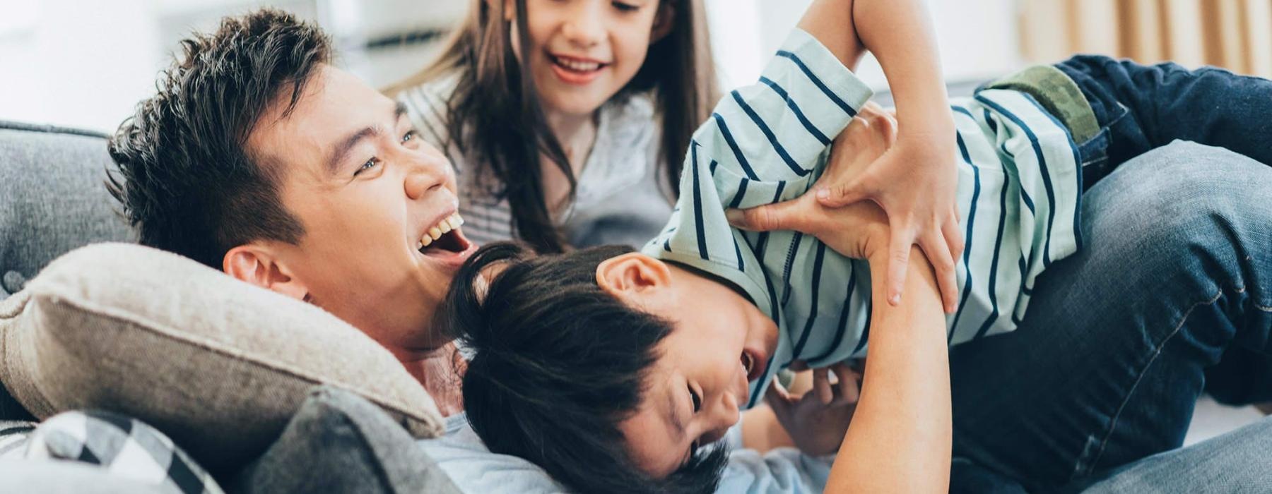 father plays on a couch with his young children